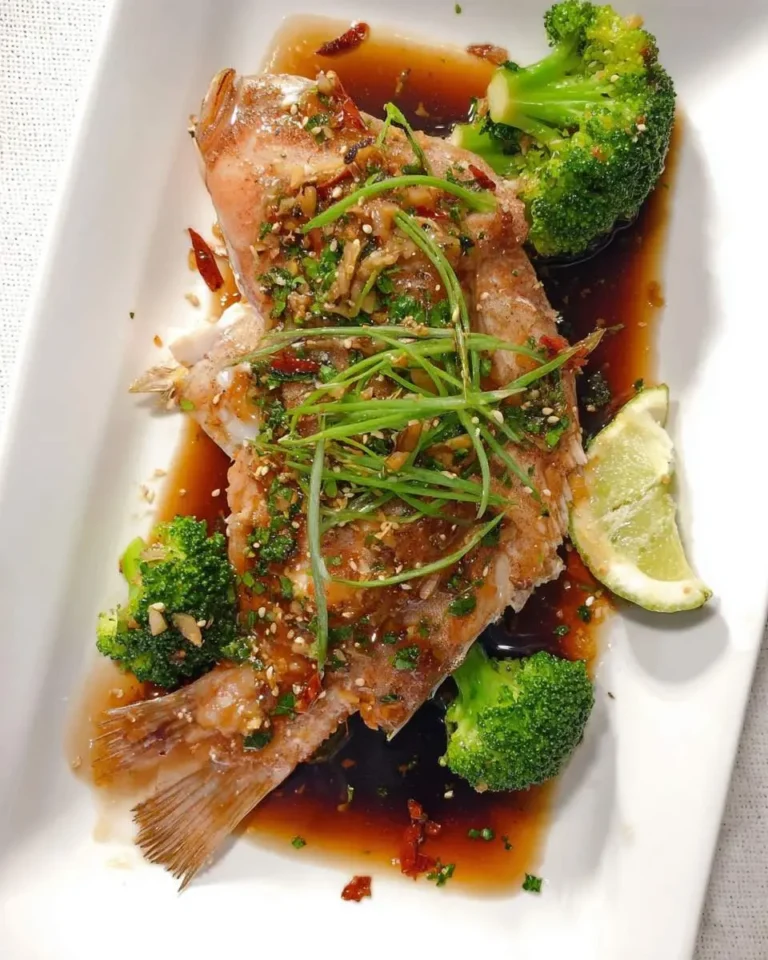 Baked Asian Rockfish served on a white plate with broccoli, lime wedge, and savory soy-based sauce garnished with scallions.