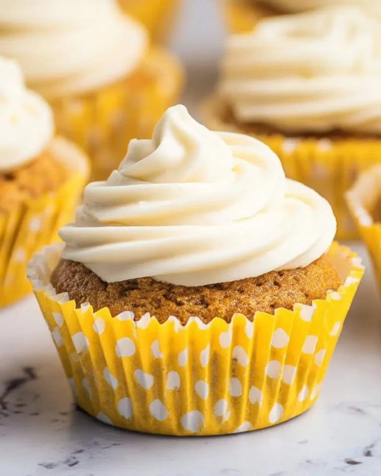 A moist banana muffin with cream cheese frosting swirled on top, wrapped in a yellow polka dot liner.