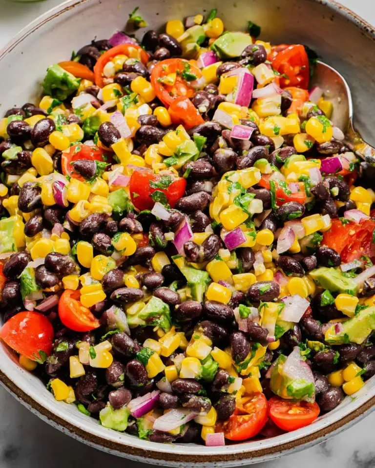 A colorful bowl of black bean salad with corn, tomatoes, avocado, and red onion mixed with fresh herbs.