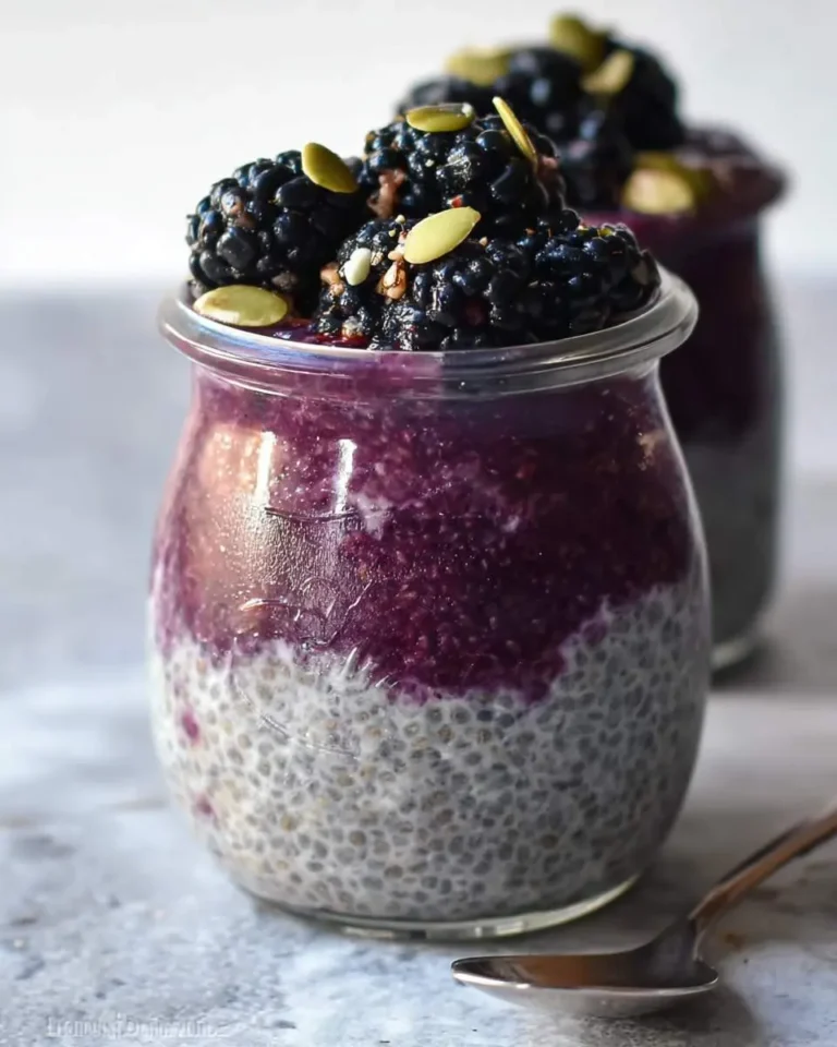 Two glass jars filled with layered blackberry chia pudding topped with fresh blackberries and pumpkin seeds.