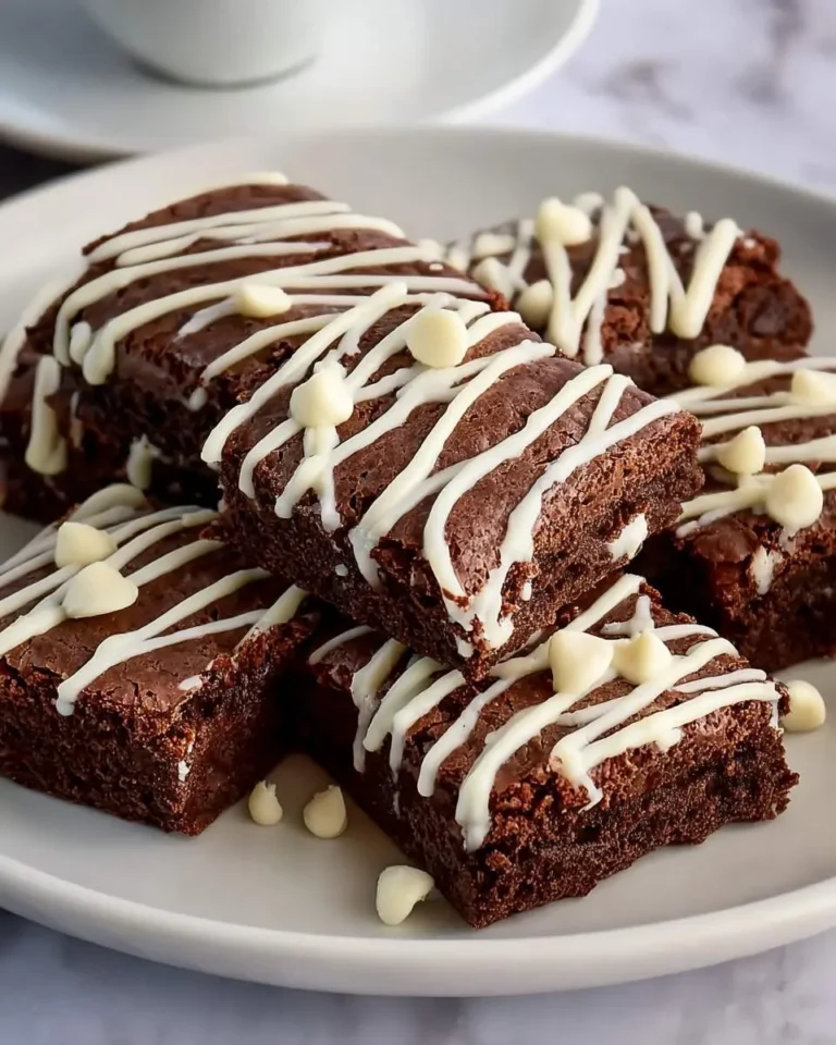 Stack of rich brownies with white chocolate chips drizzled on top, served on a white plate.