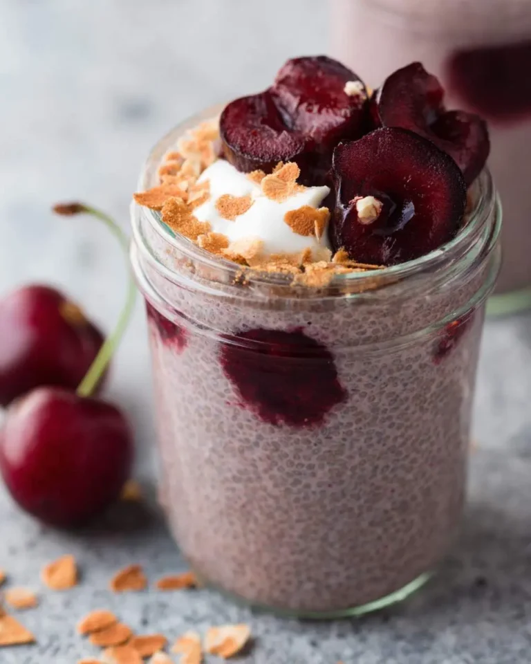 Cherry chia pudding in a glass jar topped with fresh cherries, yogurt, and crunchy coconut flakes.