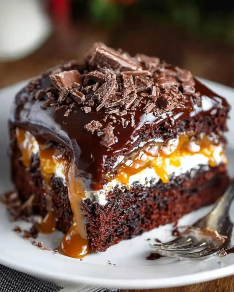 Decadent slice of Chocolate Caramel Cake topped with ganache, chocolate shavings, and dripping caramel sauce on a white plate.
