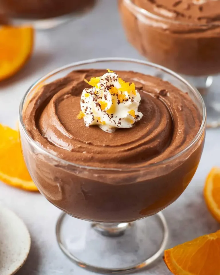 Chocolate orange mousse in a glass dessert cup topped with whipped cream and orange zest.