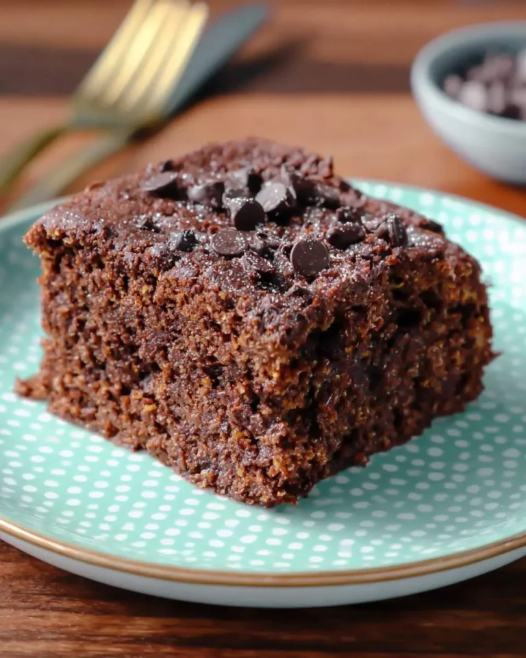A slice of moist chocolate zucchini cake topped with chocolate chips on a teal polka dot plate.