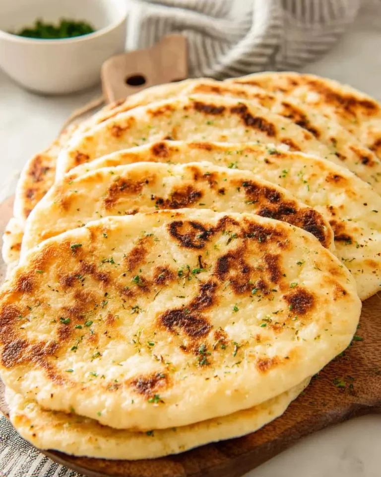 Stack of golden brown Cottage Cheese Flatbread topped with fresh herbs on a wooden board.