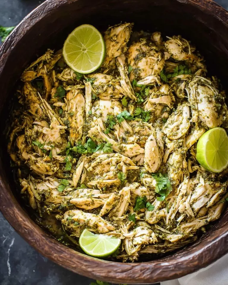Shredded Crockpot Cilantro Lime Chicken in a wooden bowl with fresh lime wedges and chopped cilantro.