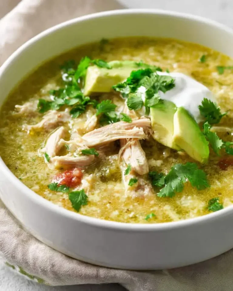 A bowl of crockpot green enchilada chicken soup topped with avocado, cilantro, and sour cream.