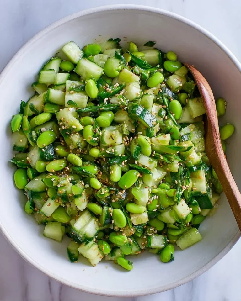 Fresh Cucumber Edamame Salad with sesame seeds and green onions in a white bowl with a wooden spoon.