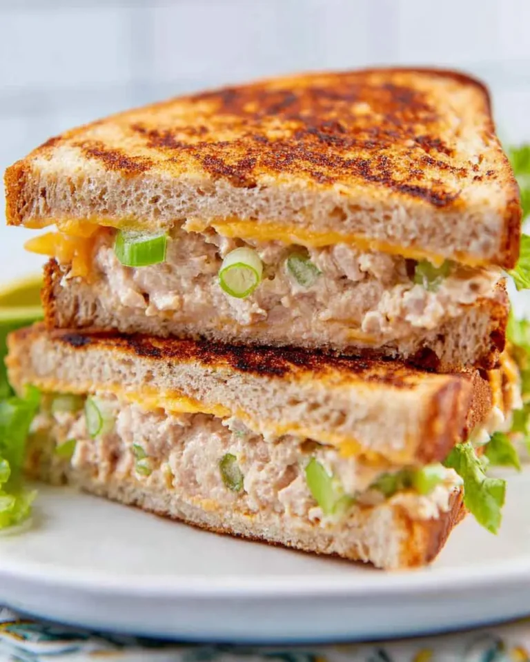 Two halves of a grilled tuna sandwich stacked on a white plate, showing melted cheese and green onions inside.