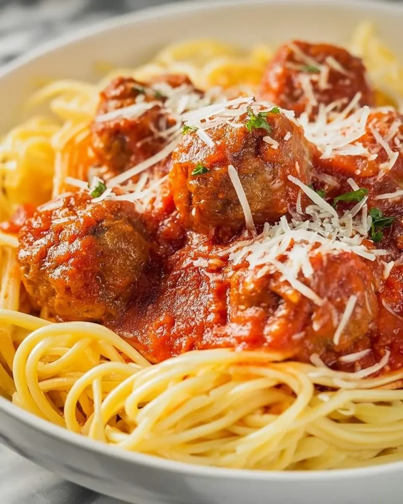 Italian Meatballs on Parmesan Noodles served in a white bowl with marinara sauce and fresh herbs.