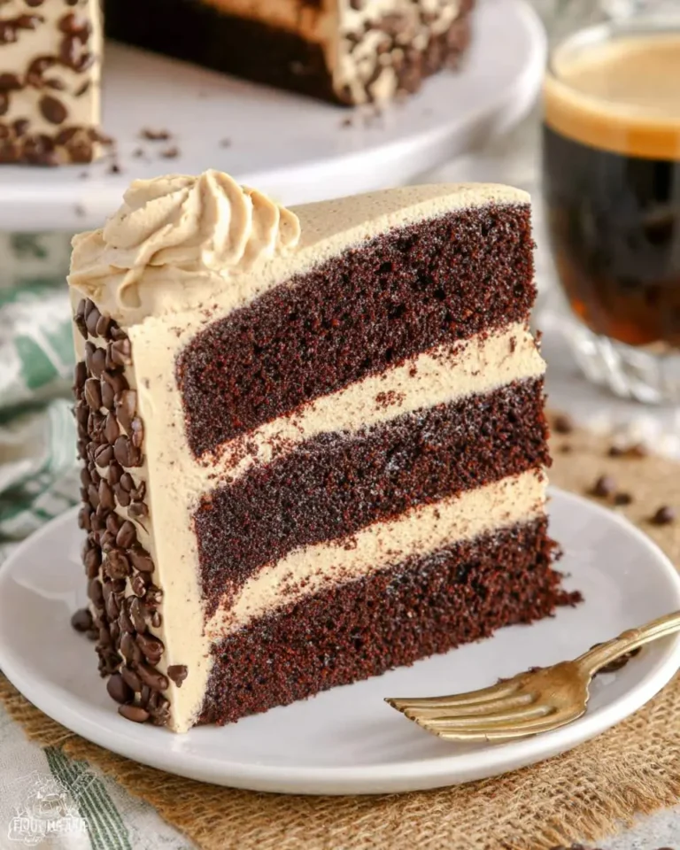 A slice of Kahlua Coffee Chocolate Layer Cake with three dark chocolate layers, coffee buttercream, and chocolate chips on a white plate.