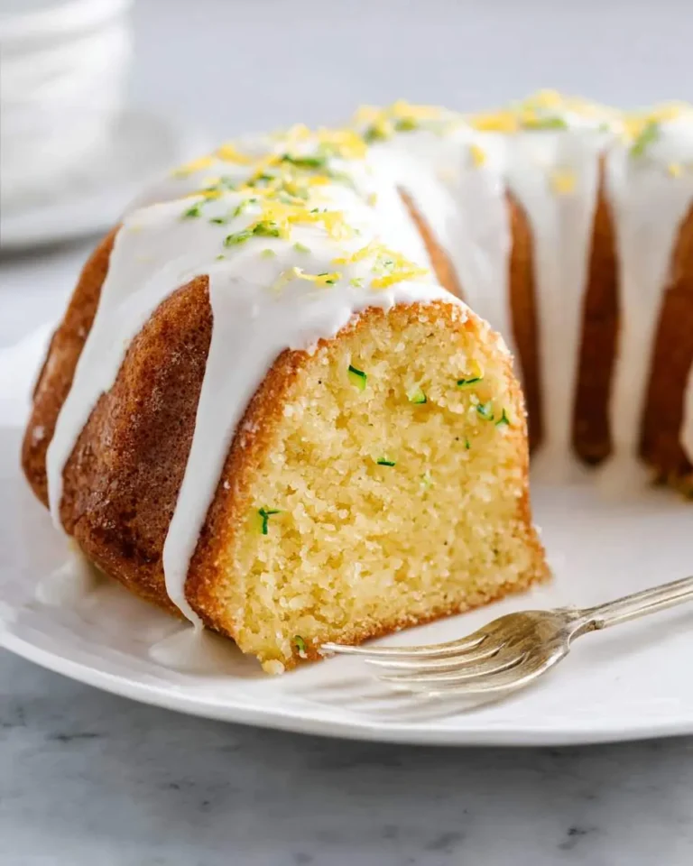 A sliced lemon zucchini bundt cake with white glaze and citrus zest on a white plate with a fork.