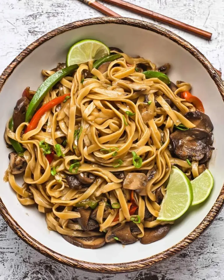 A bowl of Lo Mein with Mushrooms and Bell Peppers garnished with lime wedges and green onions.