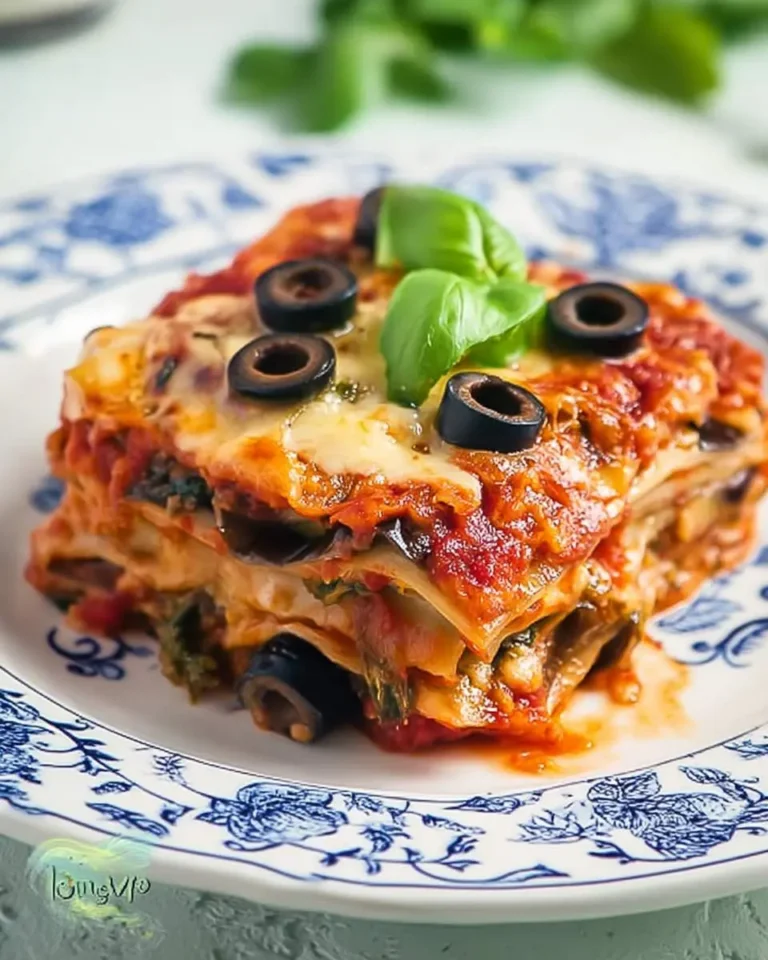 A slice of Low Carb Eggplant Lasagna topped with melted cheese, black olives, and fresh basil on a decorative blue and white plate.