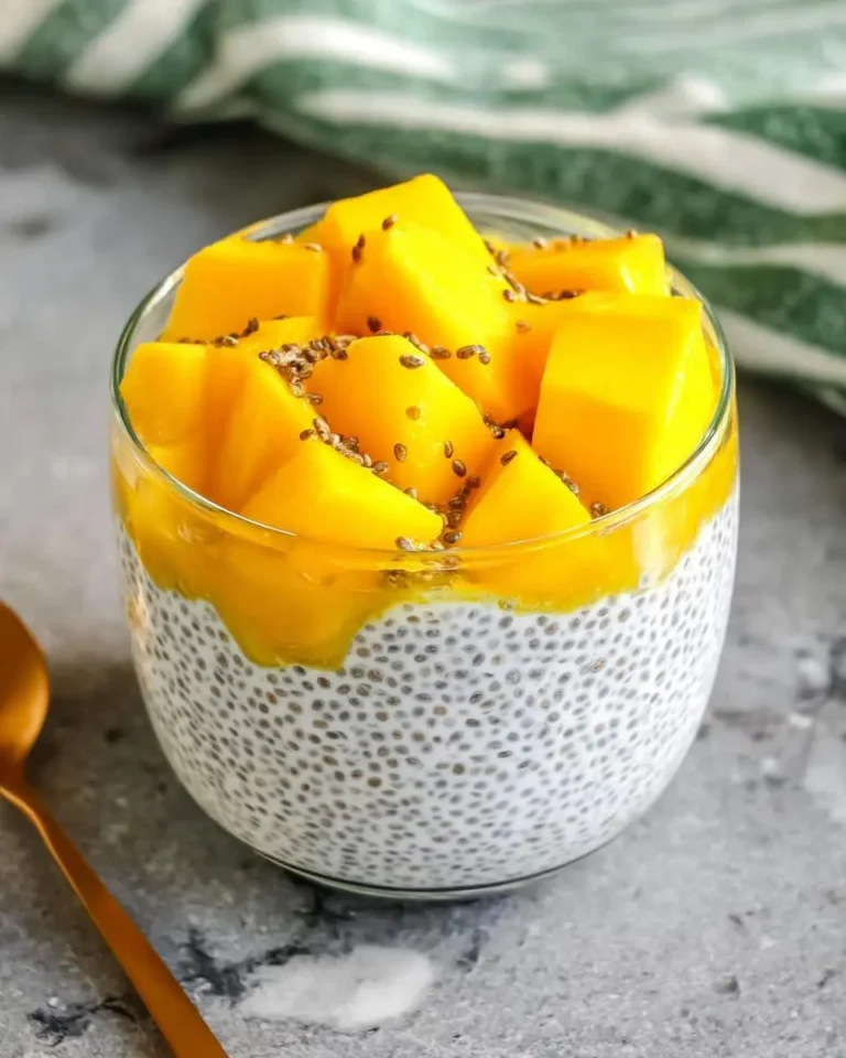 A glass jar filled with creamy mango coconut chia pudding topped with fresh mango chunks and chia seeds.