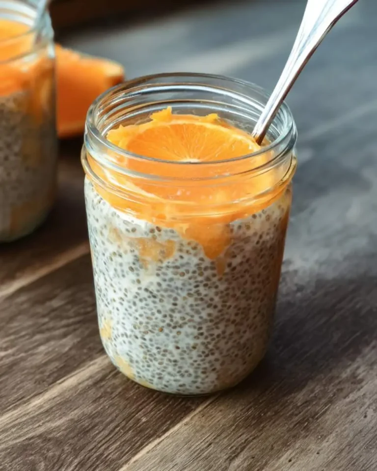Orange chia seed pudding in a glass mason jar topped with fresh orange slices and a spoon.