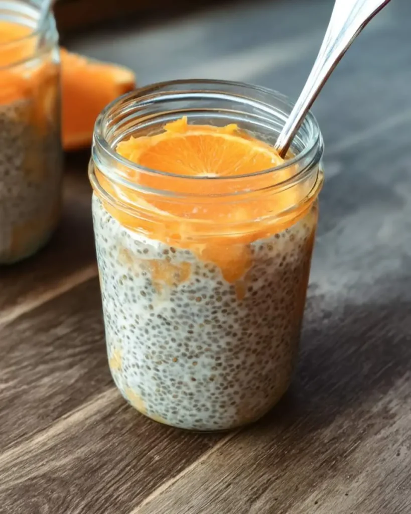 Orange chia seed pudding in a glass mason jar topped with fresh orange slices and a spoon.