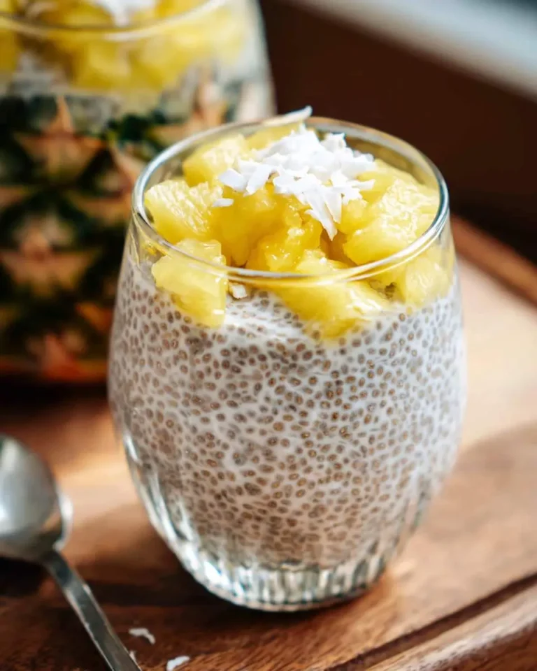 A glass jar filled with creamy pineapple chia pudding topped with fresh pineapple chunks and coconut flakes.