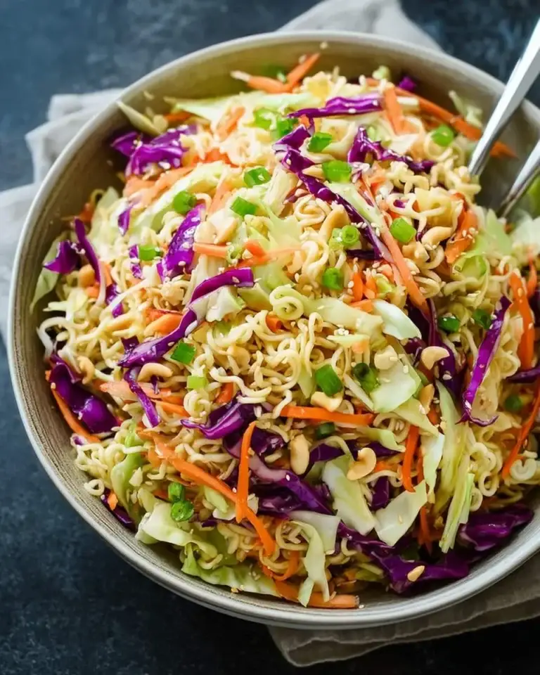 A large bowl of Ramen Noodle Salad with Cabbage featuring green and purple cabbage, carrots, green onions, peanuts, and sesame seeds.