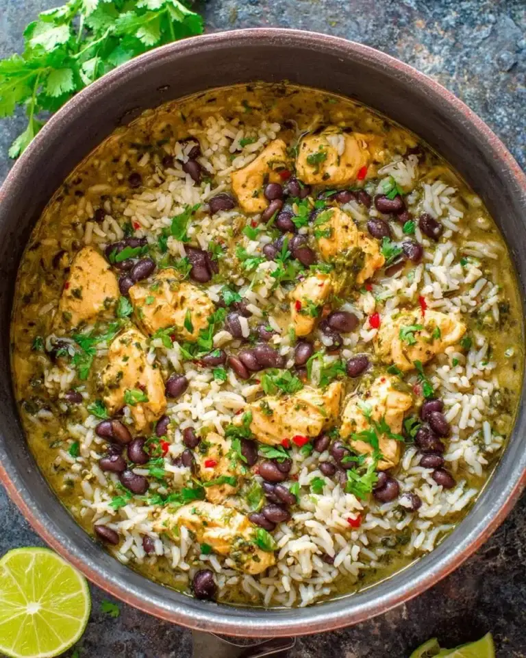 A pot of Salsa Verde Chicken, Rice, and Beans garnished with cilantro and lime on a rustic surface.