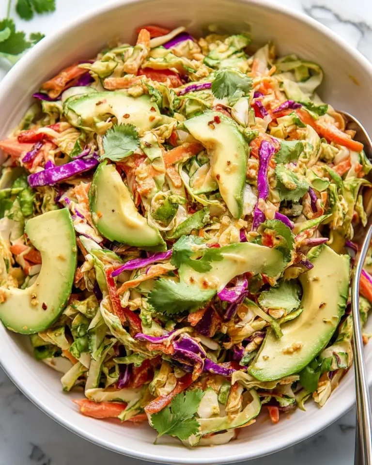 A bowl of colorful Shredded Thai Salad with Avocado, featuring cabbage, carrots, red peppers, cilantro, and a creamy dressing.