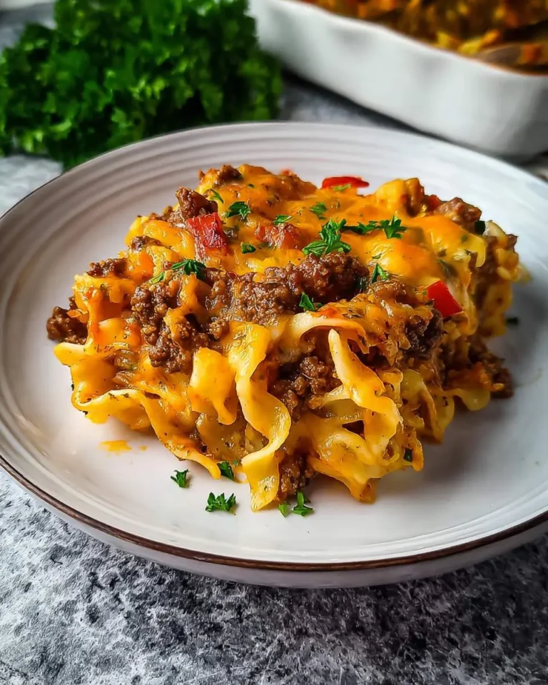 A serving of Sour Cream Beef Noodle Casserole on a white plate, topped with melted cheese and fresh parsley.