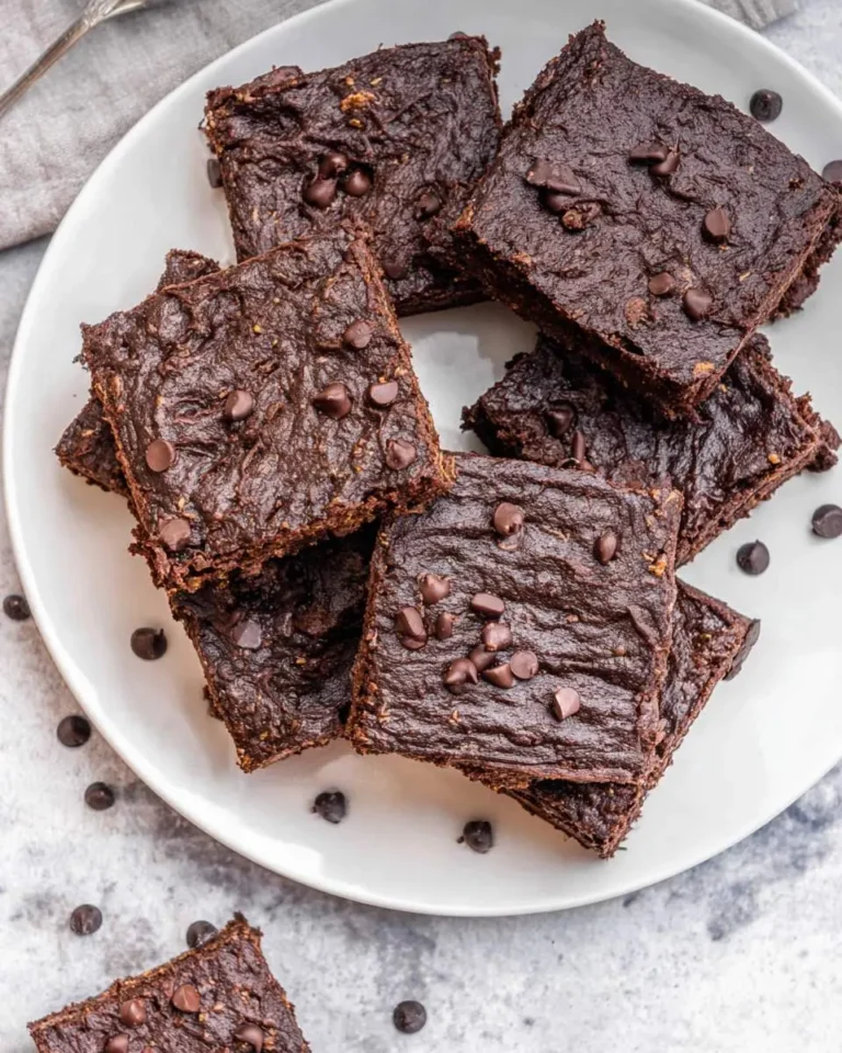 A white plate stacked with fudgy sweet potato brownies topped with chocolate chips on a gray countertop.