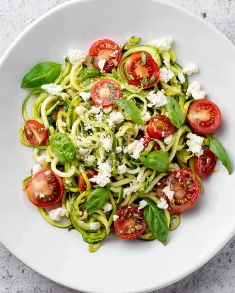 Fresh Zoodles with Summer Vegetables topped with cherry tomatoes, basil, and crumbled feta cheese in a white bowl.