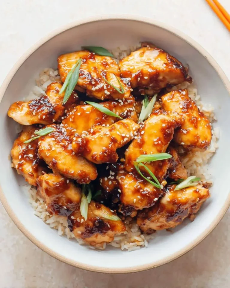 Air fryer teriyaki chicken served over rice in a bowl, garnished with sesame seeds and green onions.