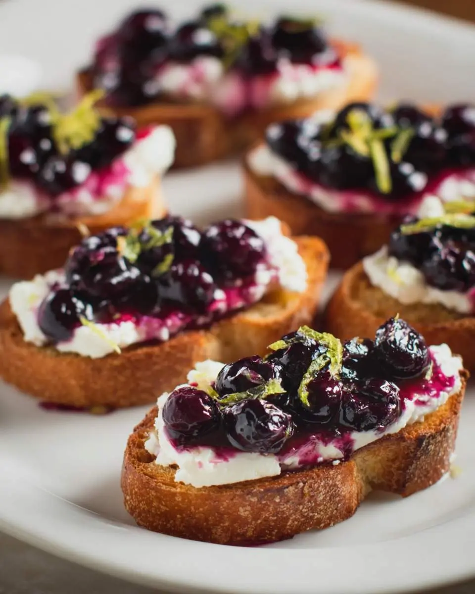 Blueberry & Goat Cheese Crostini Recipe featuring toasted bread topped with creamy goat cheese and glazed blueberries with lime zest.