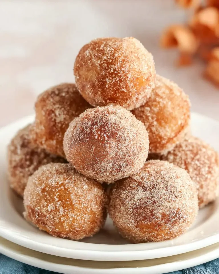 A stack of golden brown Cinnamon Sugar Donut Holes coated in sweet cinnamon sugar, piled on a white plate.