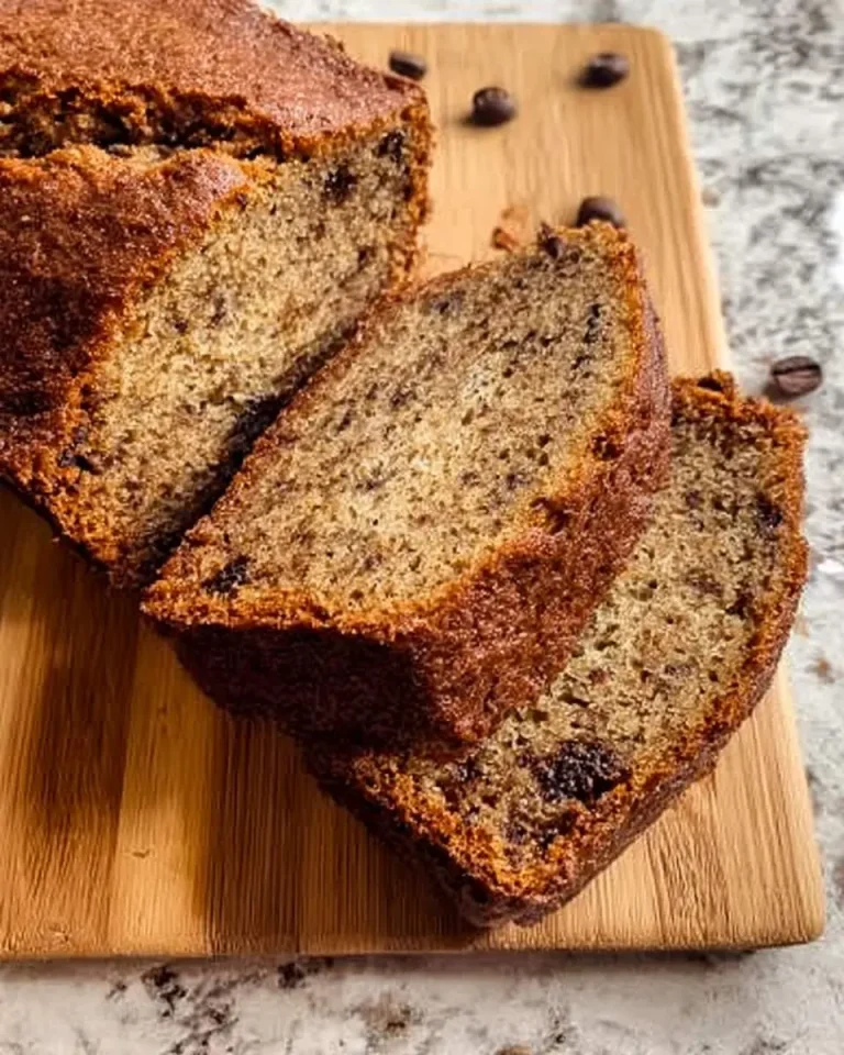 Sliced loaf of moist Coffee Banana Bread on a wooden cutting board with scattered coffee beans.