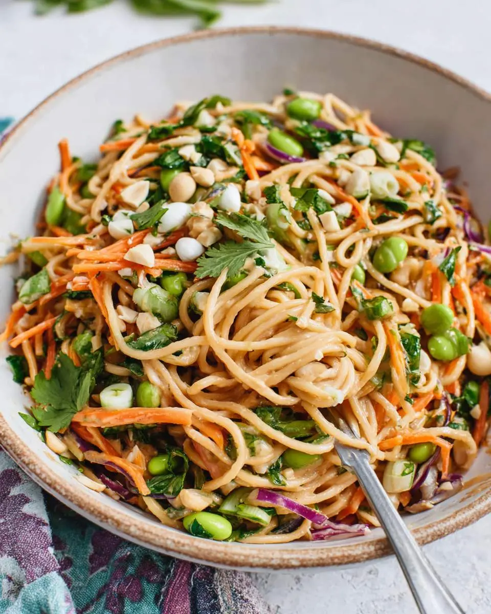 Cold Peanut Noodle Salad with spaghetti, edamame, carrots, and peanuts in a ceramic bowl with a fork.