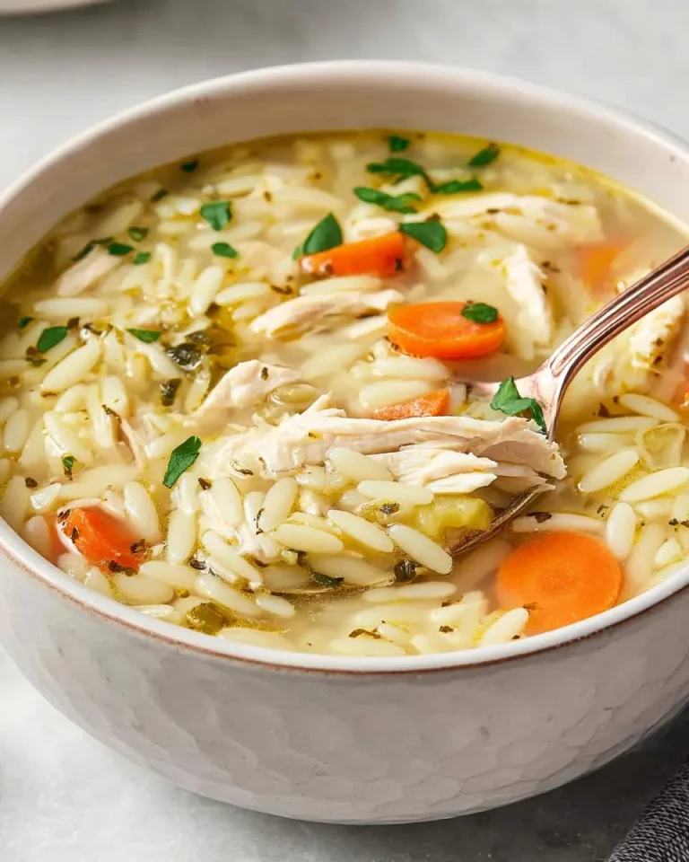 A bowl of creamy turkey orzo soup with shredded turkey, carrots, and fresh herbs in a white ceramic bowl with a spoon.