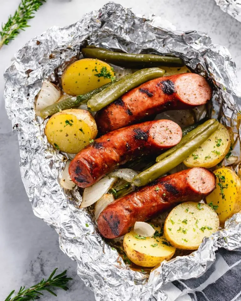 Grilled Kielbasa Foil Packets with potatoes, green beans, and onions served in an open foil wrap.