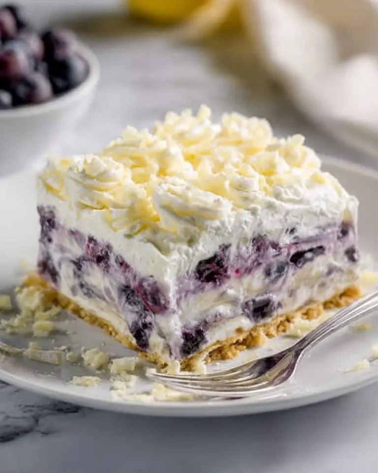 A slice of Lemon Blueberry Lasagna with creamy layers, fresh blueberries, and white chocolate shavings on a graham cracker crust.