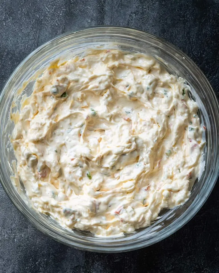 Creamy Million Dollar Crack Dip Recipe mixture in a clear glass bowl on a dark surface.