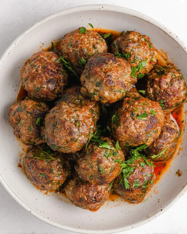 A bowl of Moroccan Lamb Meatballs garnished with fresh herbs in a creamy ceramic dish.