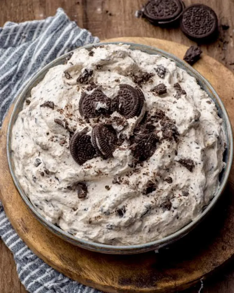 Creamy Oreo Fluff dessert topped with crushed and whole Oreo cookies in a glass bowl on a wooden board.