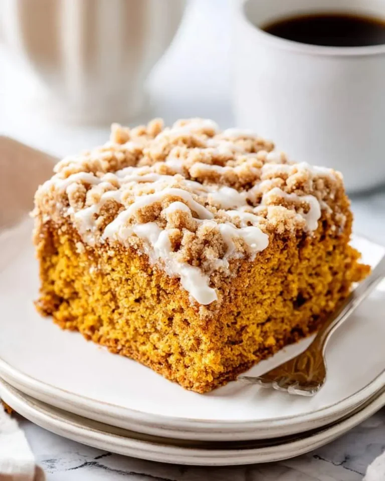 A slice of Pumpkin Crumb Coffee Cake with streusel topping and vanilla glaze on a white plate with coffee.