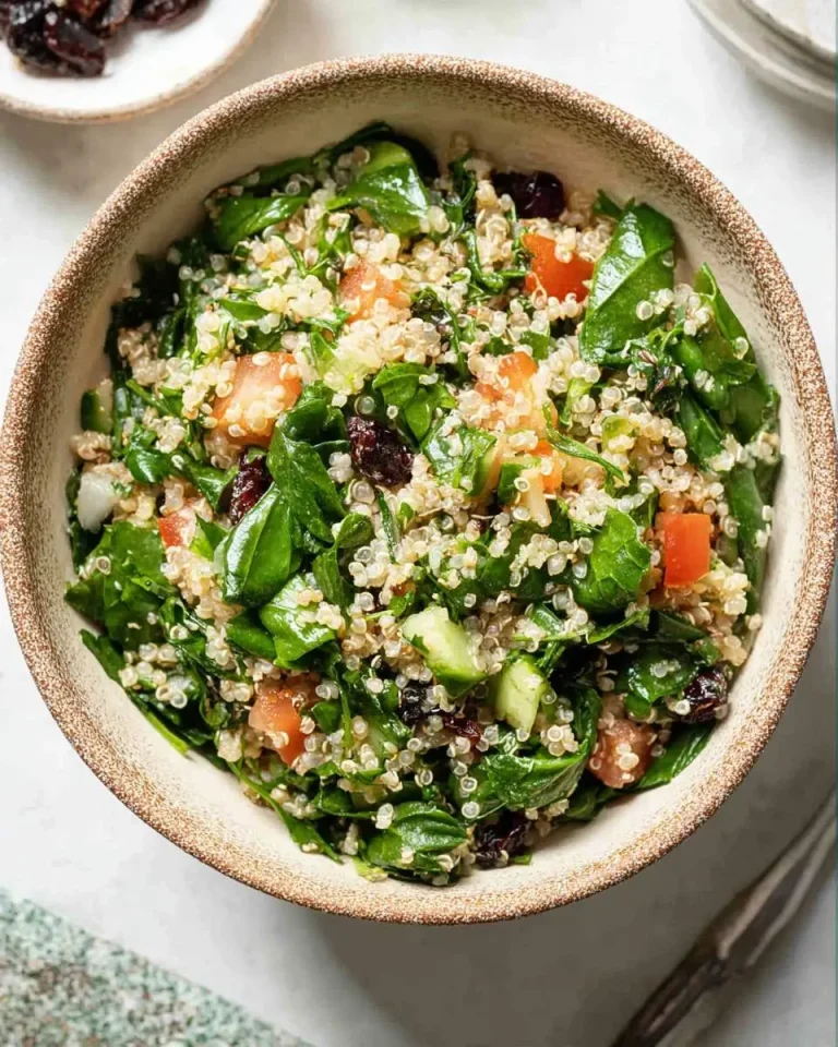 Quinoa Spinach Power Salad served in a rustic ceramic bowl, featuring fresh spinach, diced tomatoes, cucumbers, and dried cranberries.