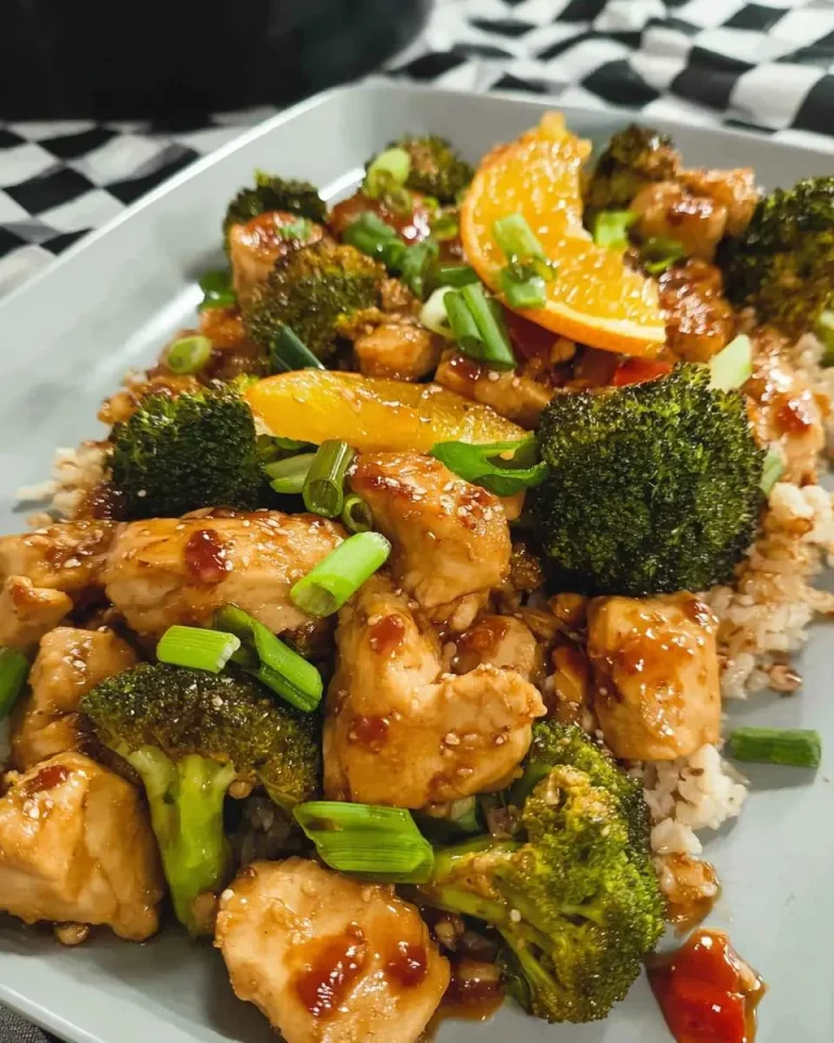 Sheet Pan Orange Chicken and Broccoli served over rice with green onions and orange slices on a gray plate.
