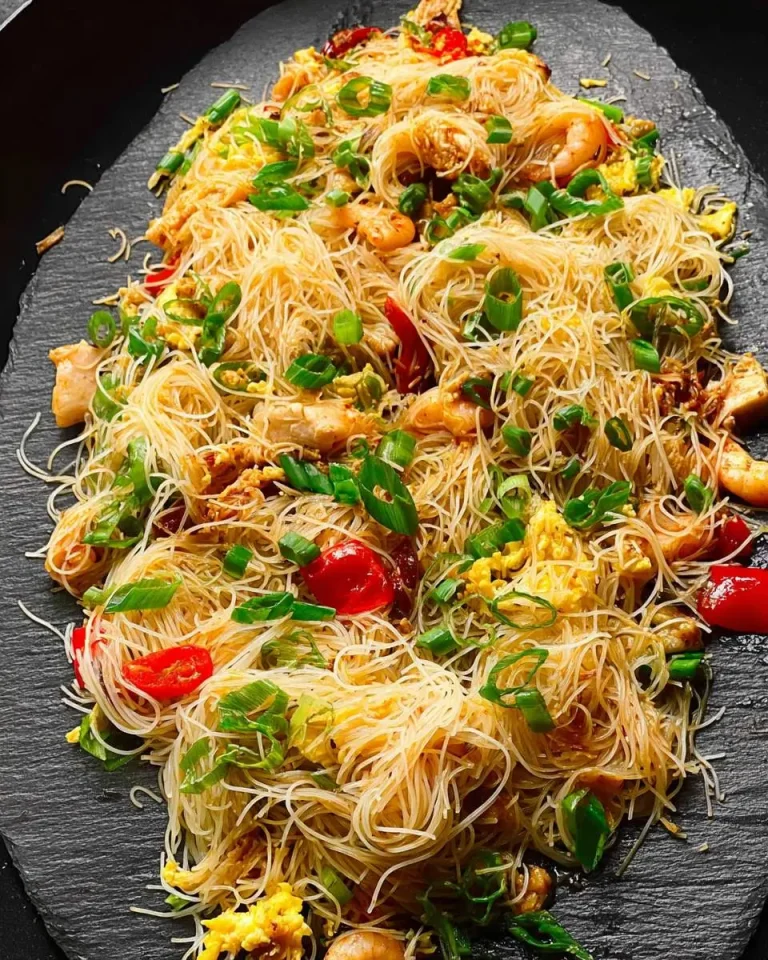 A platter of Singapore Rice Noodles with shrimp, chicken, eggs, and green onions on a black slate serving board.