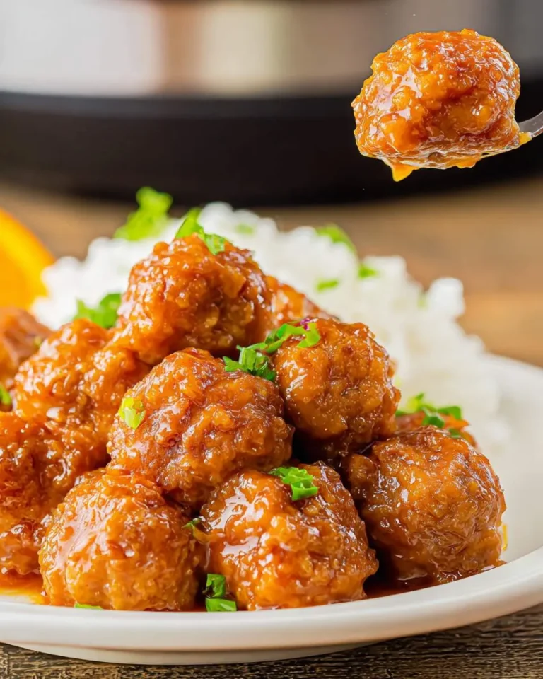 A plate of glossy Slow Cooker Orange Meatballs served over white rice, garnished with green onions, with one meatball lifted on a fork.