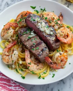 Steak and Shrimp Scampi served over linguine pasta in a white bowl, topped with garlic butter and fresh parsley.