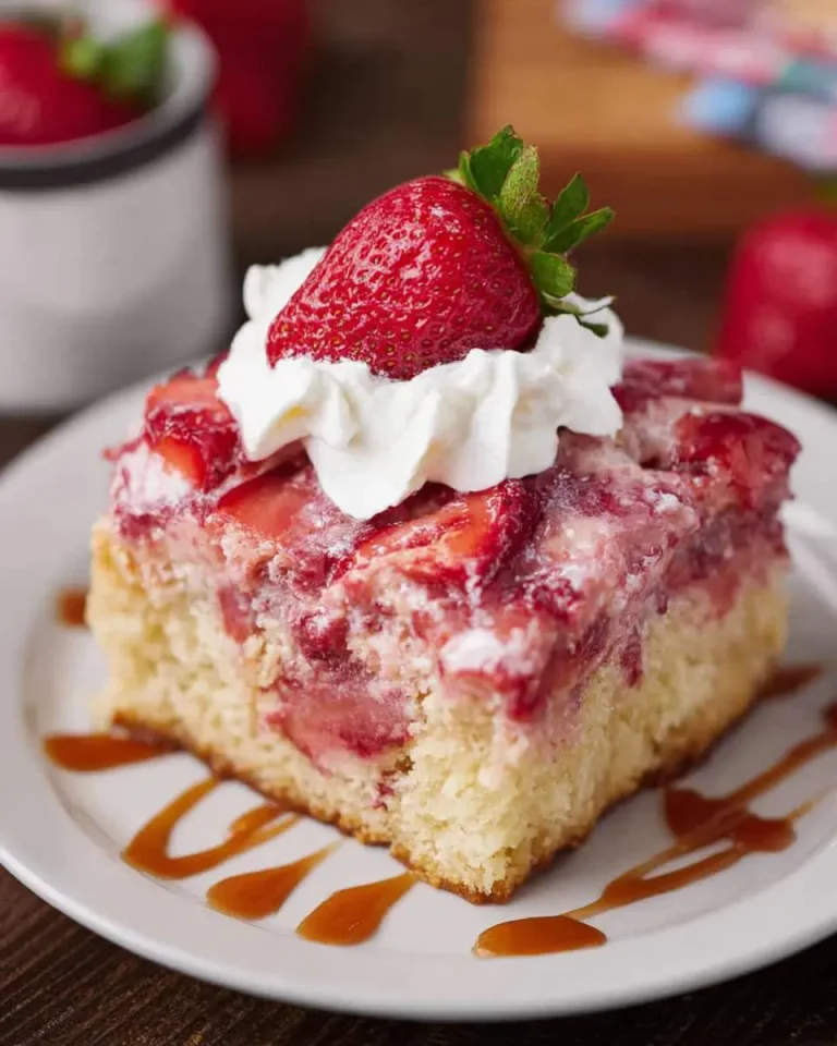 A slice of Strawberry Poke Cake topped with whipped cream and fresh strawberry on a white plate with caramel drizzle.