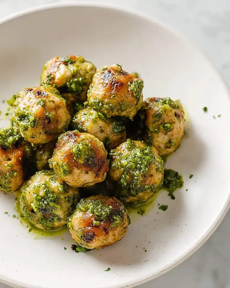 Golden brown Turkey Pesto Meatballs coated in vibrant green pesto sauce, served in a white bowl.