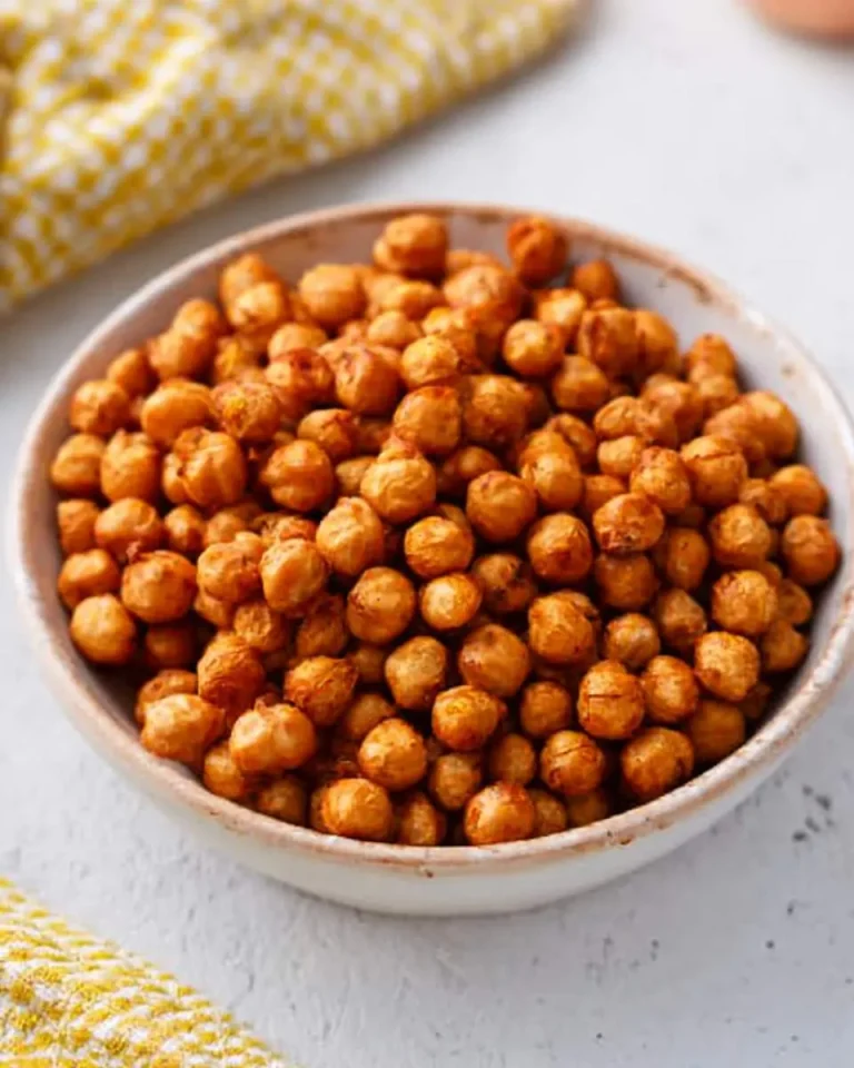 A bowl of crispy golden Air Fryer Chickpeas on a light surface with yellow patterned cloth nearby.