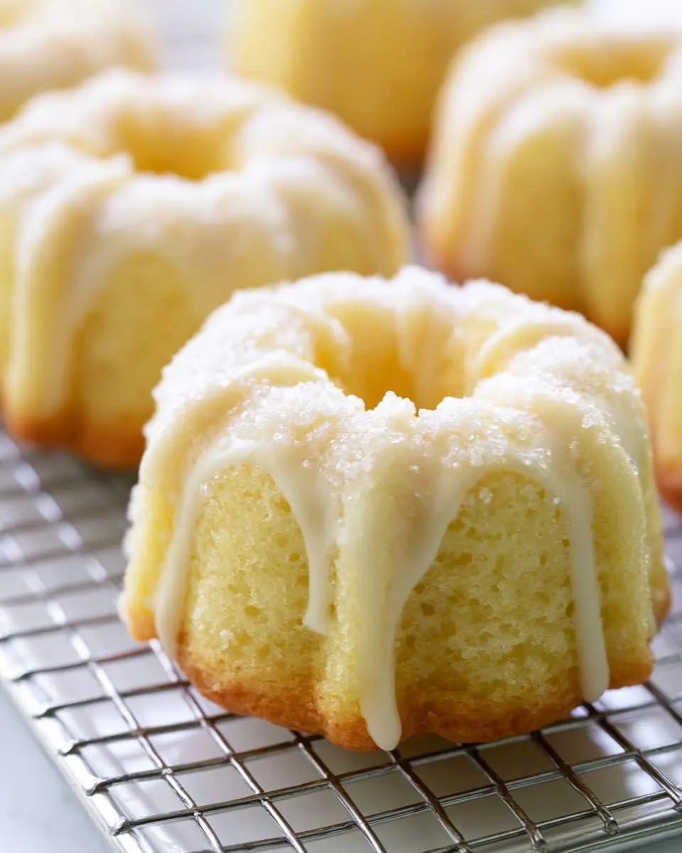 Mini Lemon Bundt Cakes with white glaze and sugar crystals cooling on a wire rack.